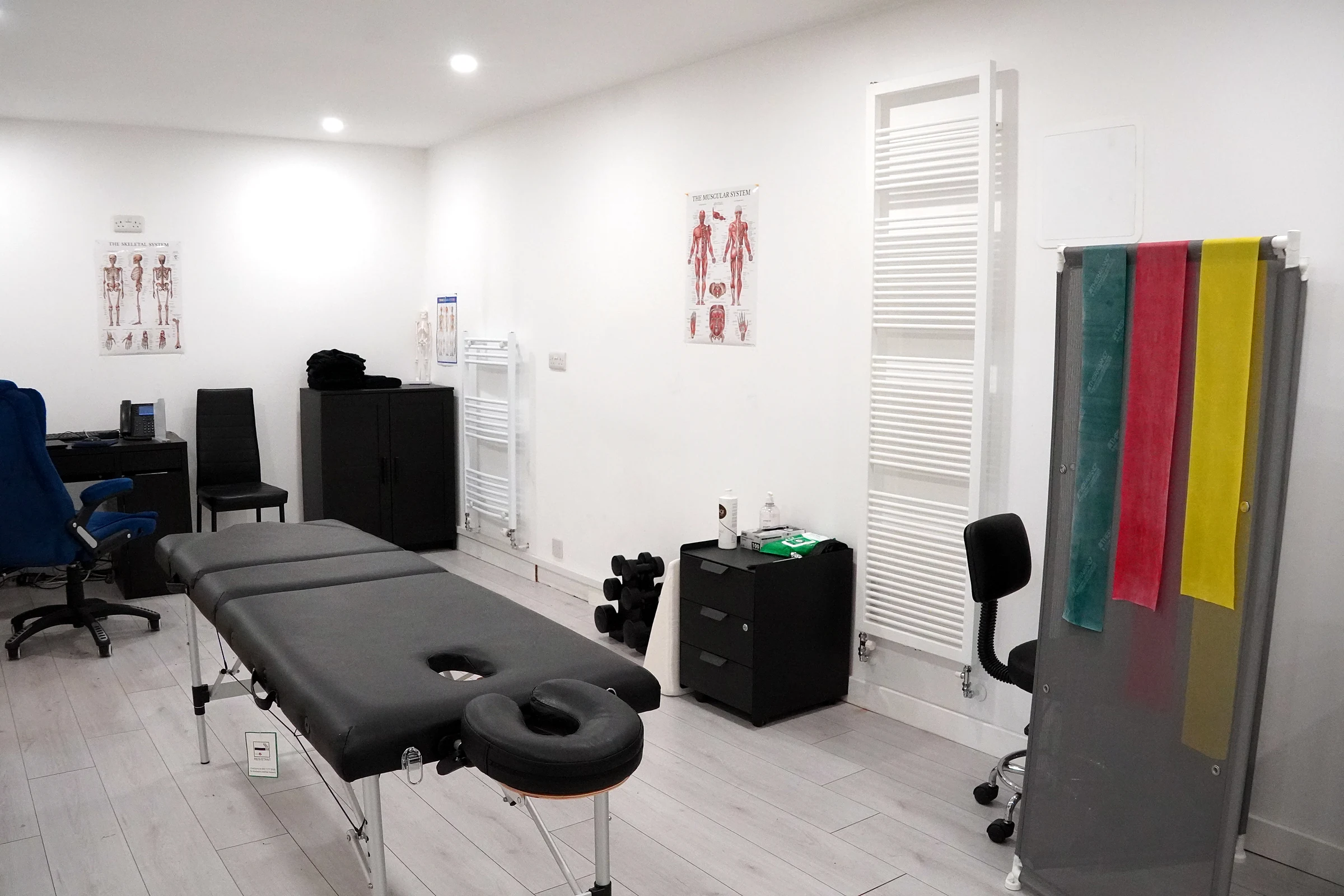The Physio Source treatment room, with a treatment couch, anatomy posters and resistance bands